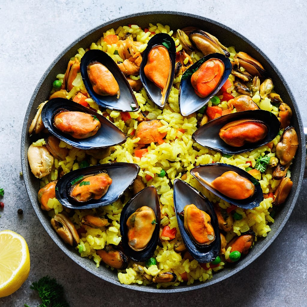 Traditional spanish seafood paella in pan rice, peas, shrimps, mussels, squid on light grey concrete