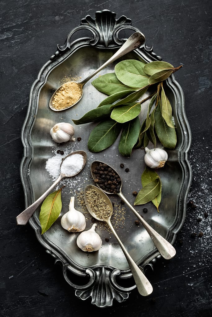 Dark culinary background with bay leaves, salt, pepper and garlic