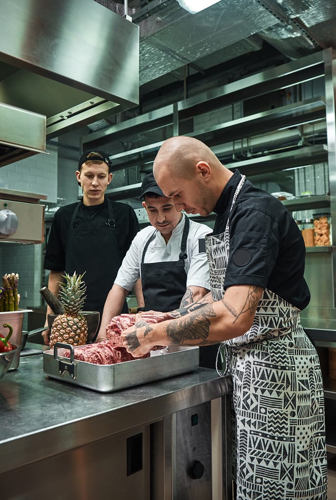 Culinary school. Professional chef with tattoos on his hands holding a red meat and teaching
